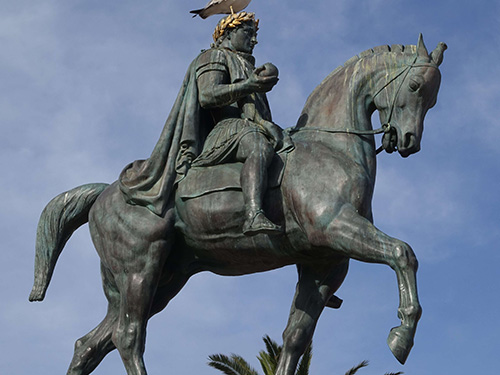 A bird standing on the head of a bronze statue of Napoleon in Ajaccio, Corsica